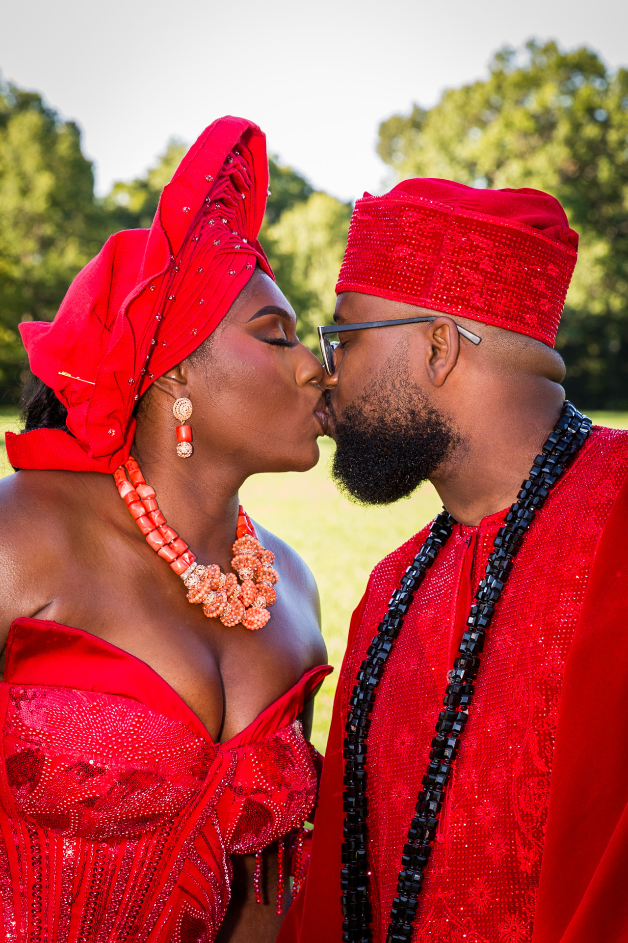A couple in red traditional wedding attire sharing a kiss outdoors